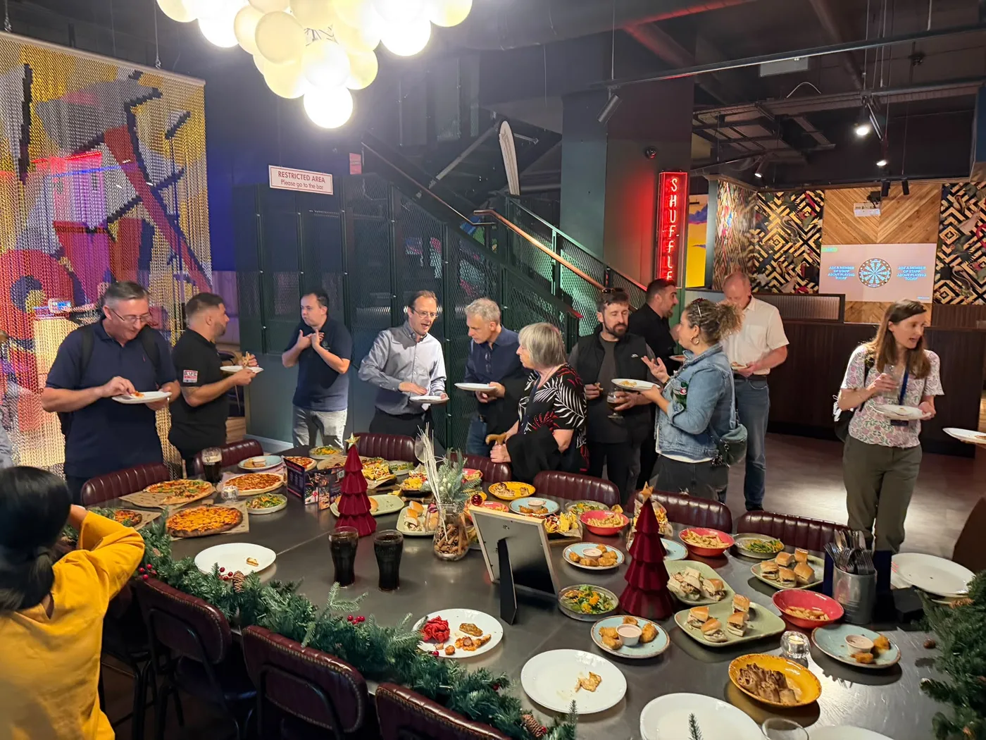 Guild members serving themselves from a long table of food decorated with small Christmas trees